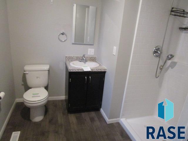 bathroom with wood finished floors, toilet, vanity, baseboards, and a stall shower