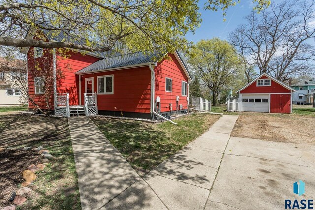 exterior space featuring a garage, driveway, an outdoor structure, metal roof, and a wooden deck