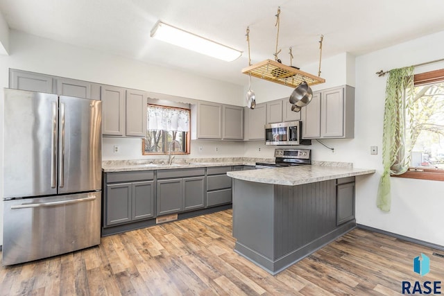 kitchen featuring stainless steel appliances, wood finished floors, gray cabinets, a sink, and a peninsula
