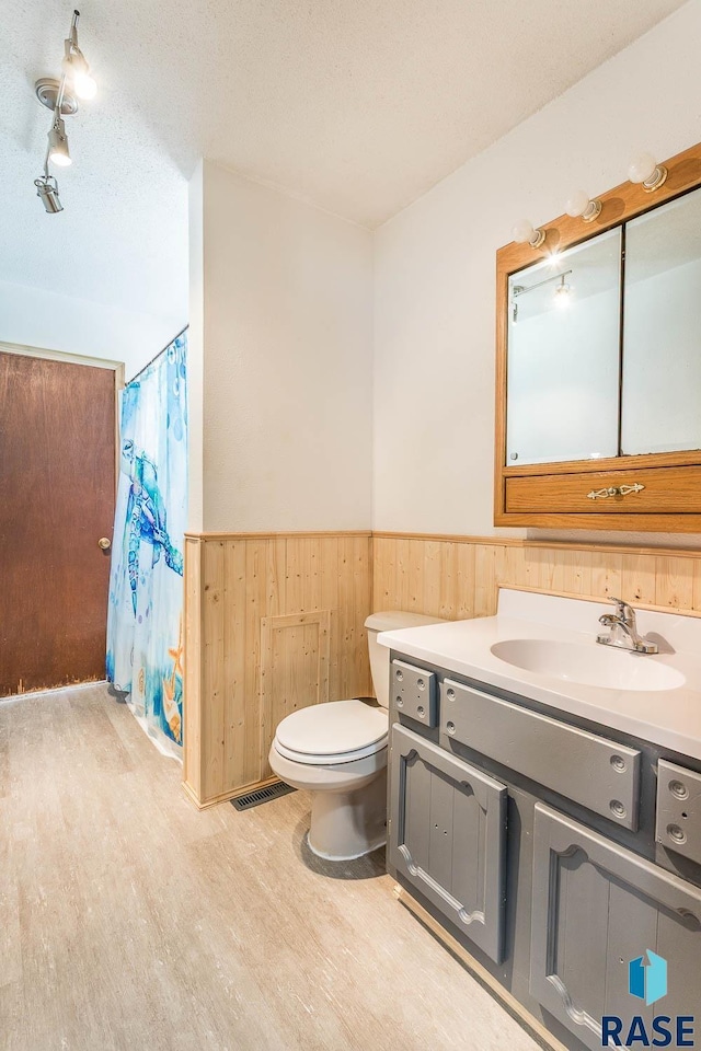 bathroom featuring a wainscoted wall, a shower with curtain, toilet, wood finished floors, and vanity