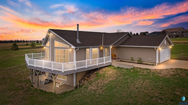 back of property with a deck, a yard, a shingled roof, and driveway