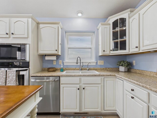 kitchen featuring glass insert cabinets, stainless steel appliances, light countertops, white cabinets, and a sink