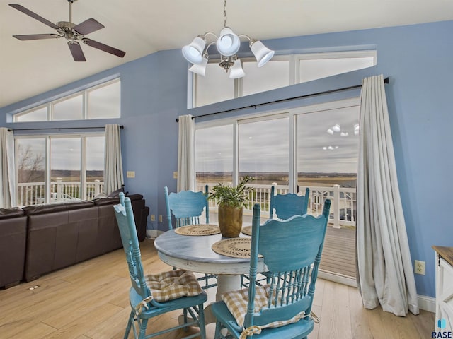 dining area with light wood finished floors, ceiling fan with notable chandelier, high vaulted ceiling, and a healthy amount of sunlight