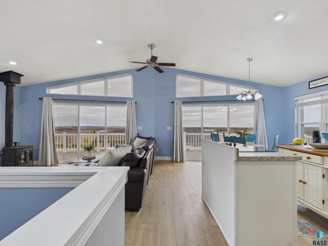 kitchen featuring white cabinets, ceiling fan, light wood finished floors, a wood stove, and lofted ceiling