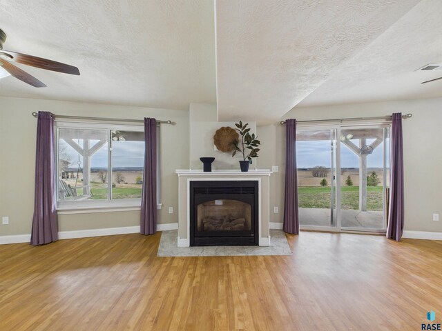 unfurnished living room with wood finished floors, plenty of natural light, visible vents, a ceiling fan, and a textured ceiling