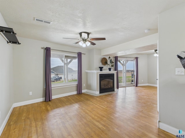 unfurnished living room featuring a healthy amount of sunlight, visible vents, a ceiling fan, and light wood finished floors