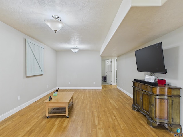 unfurnished living room with a textured ceiling, baseboards, and light wood-type flooring