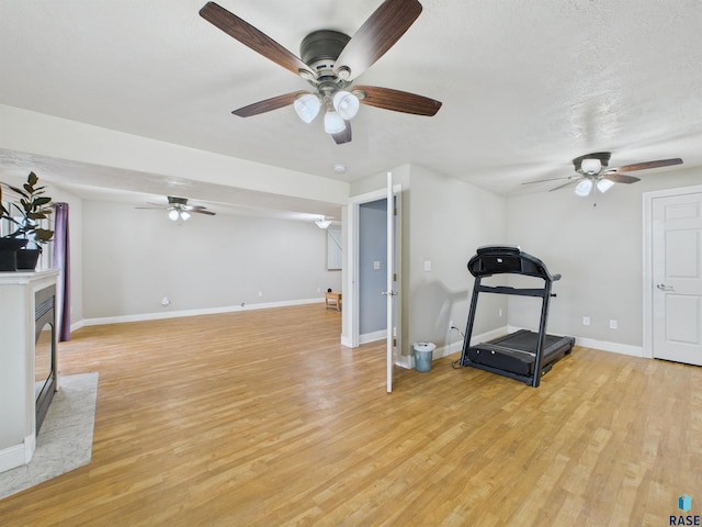 exercise room with baseboards, ceiling fan, and light wood-style flooring