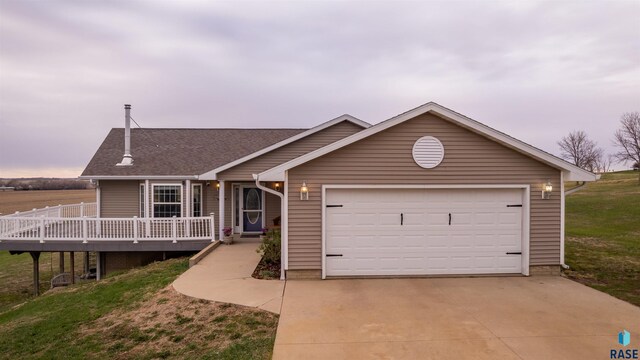 view of front facade with a front yard, a wooden deck, a shingled roof, driveway, and an attached garage