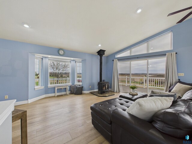 living room with wood finished floors, ceiling fan, baseboards, a wood stove, and lofted ceiling