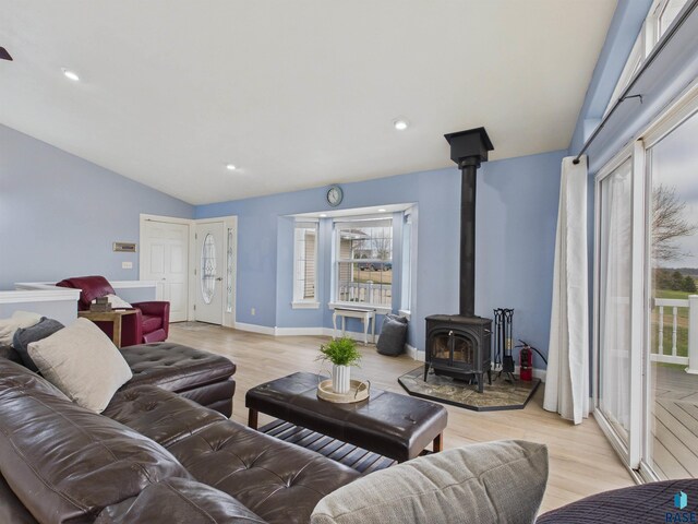 living room featuring a wood stove, recessed lighting, light wood-type flooring, vaulted ceiling, and baseboards