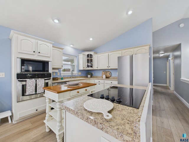 kitchen featuring light wood-type flooring, black appliances, lofted ceiling, and a kitchen island