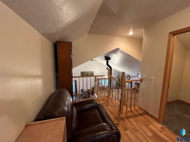 sitting room with an upstairs landing, vaulted ceiling, baseboards, a textured ceiling, and wood finished floors