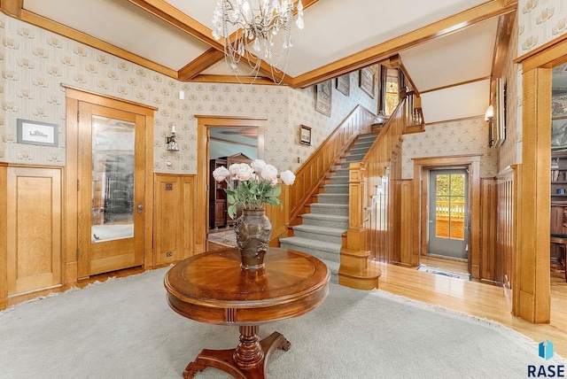 entrance foyer featuring wood finished floors, stairs, wallpapered walls, a wainscoted wall, and a notable chandelier