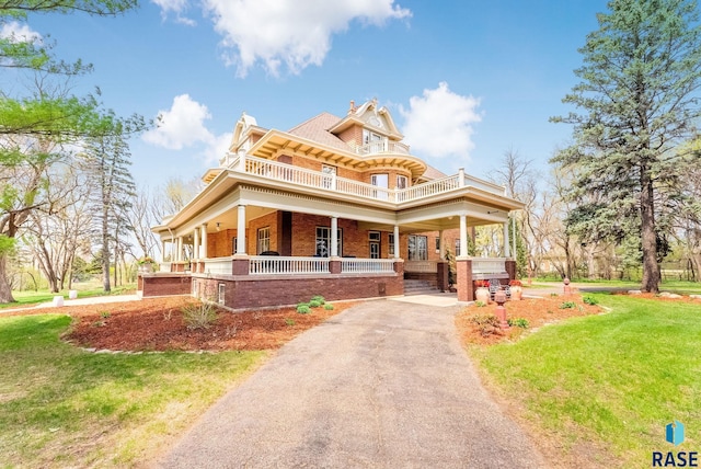 view of front of home featuring a front lawn, driveway, covered porch, and a balcony