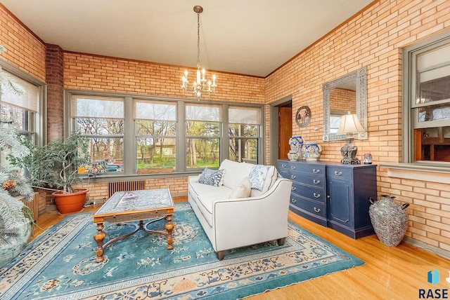 sitting room featuring radiator heating unit, wood finished floors, brick wall, and a notable chandelier