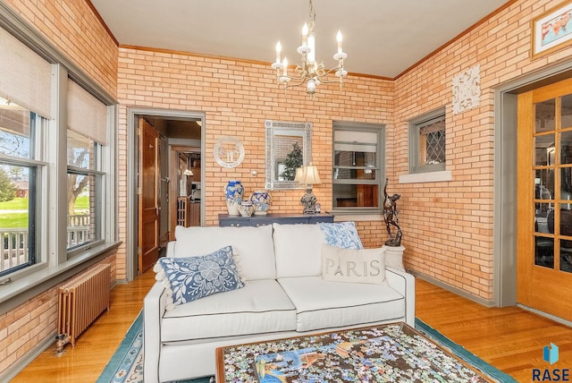 living area featuring wood finished floors, a chandelier, brick wall, and radiator