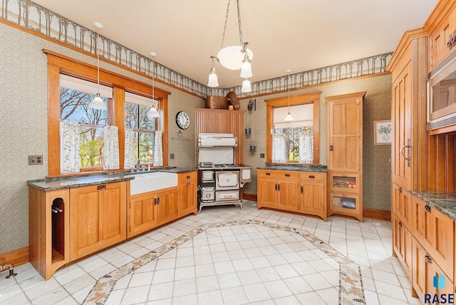 kitchen featuring hanging light fixtures, stainless steel microwave, wallpapered walls, a sink, and baseboards