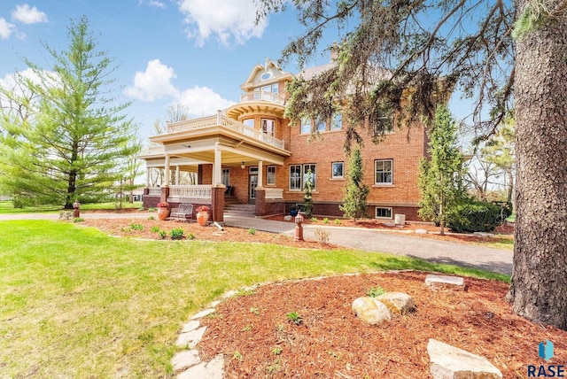 rear view of house featuring a porch, a yard, a balcony, and brick siding