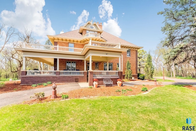 back of property with a balcony, a shingled roof, covered porch, a yard, and brick siding