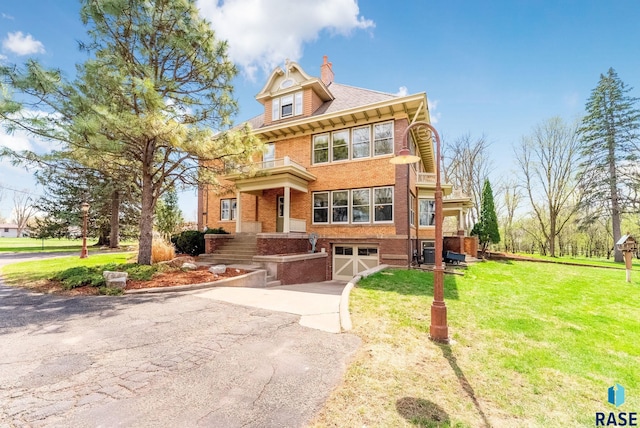 view of front of property with driveway, a balcony, a front yard, brick siding, and a garage