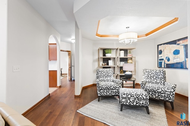 living area featuring baseboards, arched walkways, a chandelier, and a tray ceiling