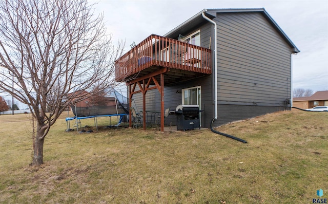 rear view of property featuring a deck, a yard, and a trampoline