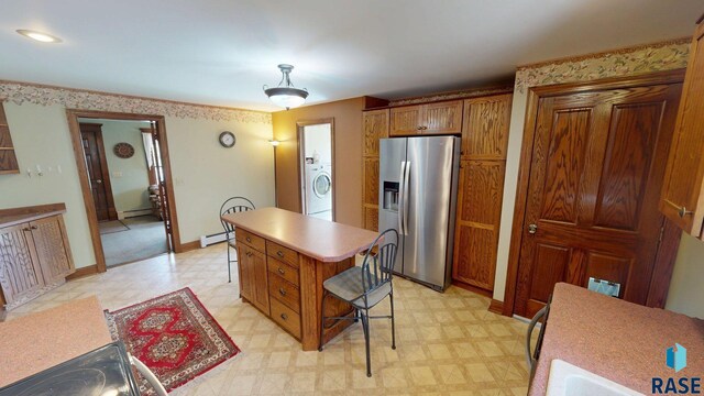 712 6th St, Brookings, SD 57006 - kitchen with a kitchen island, a baseboard heating unit, light floors, stainless steel refrigerator with ice dispenser, and washer / dryer