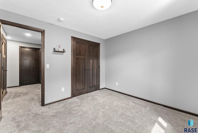 unfurnished bedroom with baseboards, light carpet, and a closet
