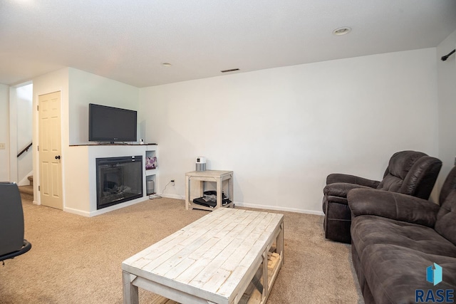 living room featuring light colored carpet, baseboards, a glass covered fireplace, and stairway