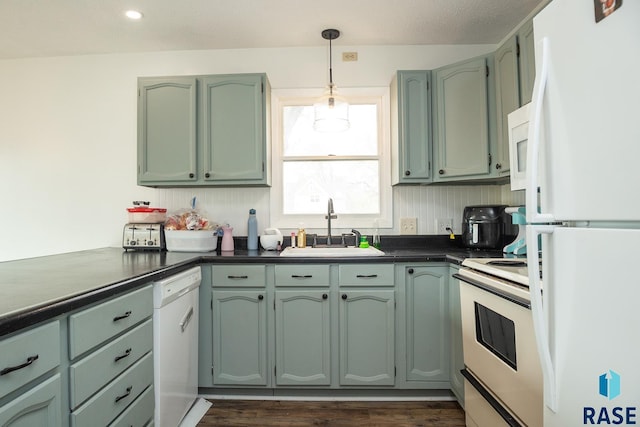 kitchen featuring dark countertops, a sink, white appliances, pendant lighting, and green cabinets