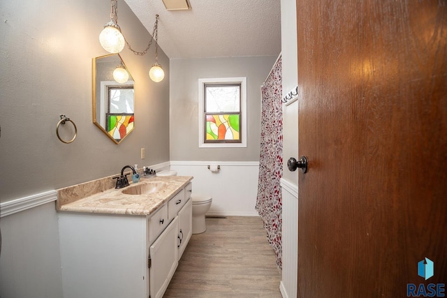 full bathroom with vanity, toilet, a textured ceiling, a wainscoted wall, and wood finished floors