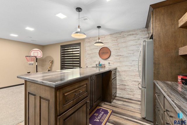 kitchen featuring dark brown cabinetry, wood walls, freestanding refrigerator, and pendant lighting