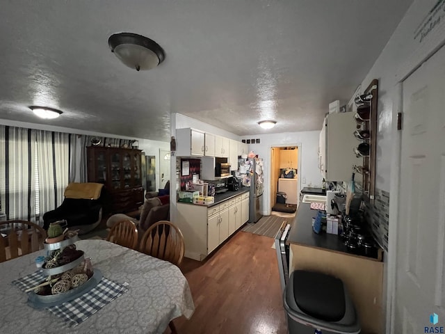 kitchen with dark countertops, a textured ceiling, white cabinets, freestanding refrigerator, and wood finished floors