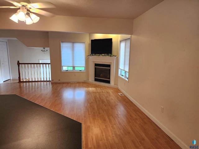 unfurnished living room with a wealth of natural light, light wood-style floors, ceiling fan, and baseboards