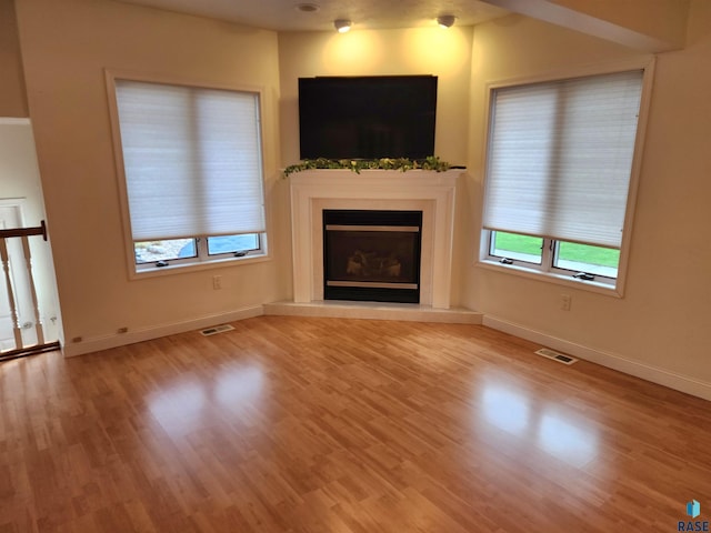 unfurnished living room with baseboards, visible vents, wood finished floors, and a glass covered fireplace
