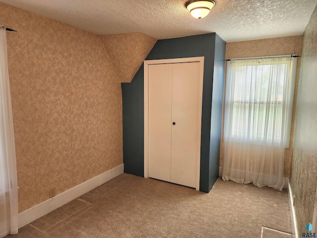 unfurnished bedroom with a textured ceiling, a closet, wallpapered walls, and carpet floors