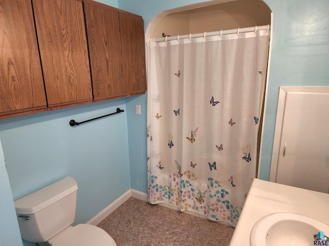 bathroom featuring toilet, a sink, baseboards, and a shower with shower curtain