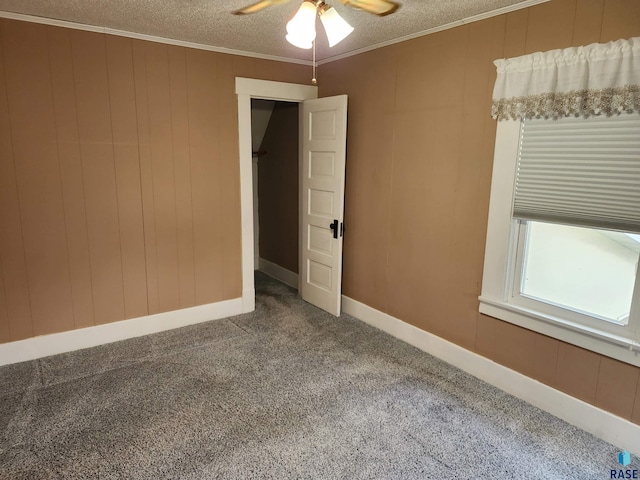 carpeted empty room featuring wood walls, a textured ceiling, a ceiling fan, and crown molding