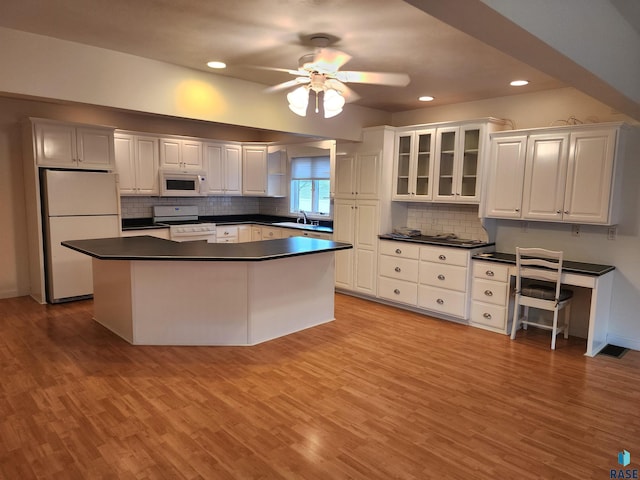 kitchen featuring dark countertops, recessed lighting, white appliances, and a sink