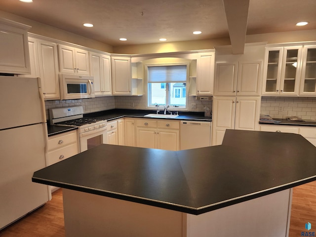 kitchen with dark countertops, white appliances, white cabinets, and a sink