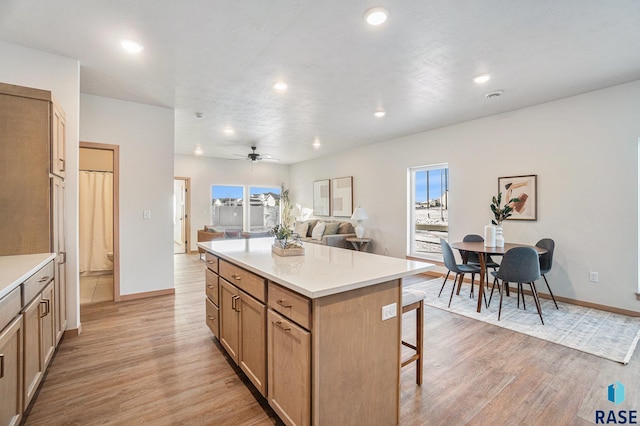 kitchen featuring light wood finished floors, a kitchen bar, ceiling fan, and open floor plan