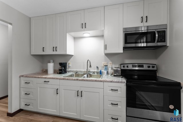 kitchen with white cabinets, light wood-style flooring, a sink, stainless steel appliances, and light countertops