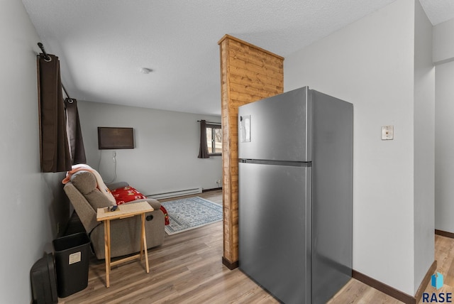 kitchen featuring a textured ceiling, baseboard heating, freestanding refrigerator, baseboards, and light wood finished floors