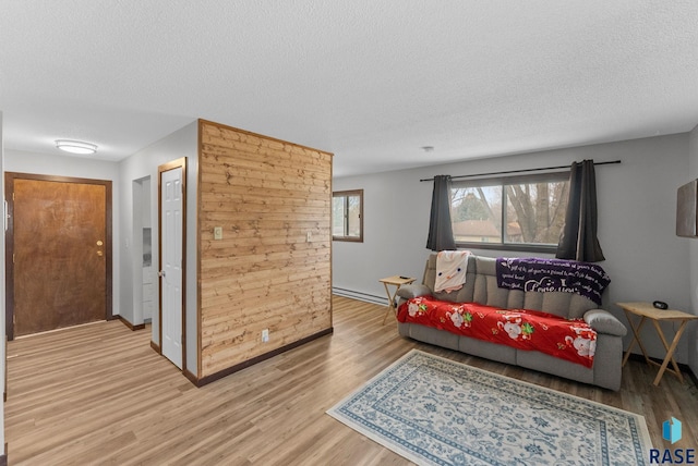 living area featuring a textured ceiling, light wood finished floors, baseboard heating, and baseboards
