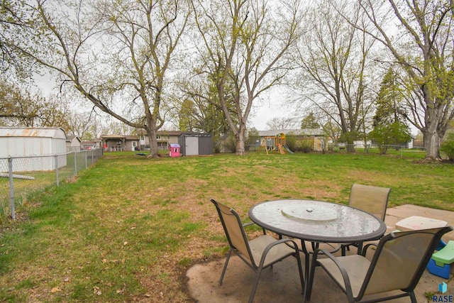 view of yard featuring an outdoor structure, a fenced backyard, a storage unit, a playground, and a patio area