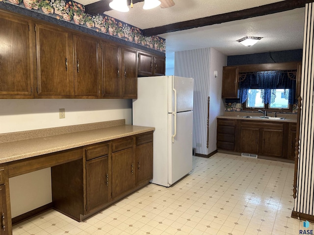 kitchen with beam ceiling, a sink, freestanding refrigerator, a ceiling fan, and light floors