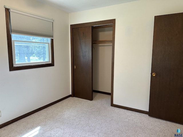 unfurnished bedroom with baseboards, light colored carpet, and a closet