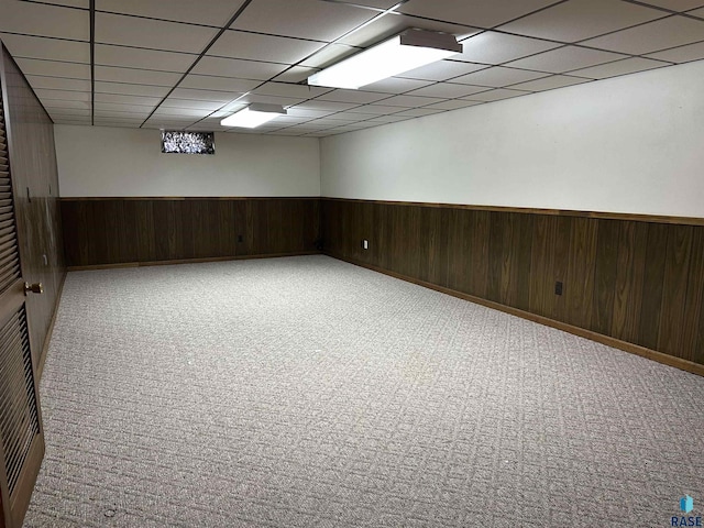 carpeted spare room featuring wooden walls, a paneled ceiling, and a wainscoted wall