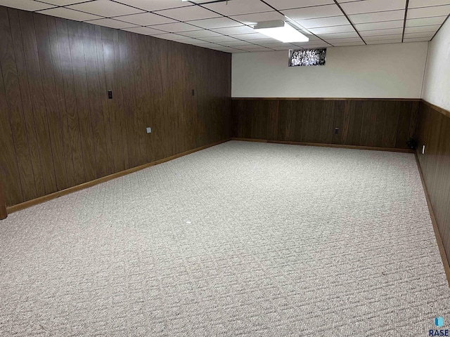 finished below grade area featuring carpet flooring, a paneled ceiling, and wooden walls